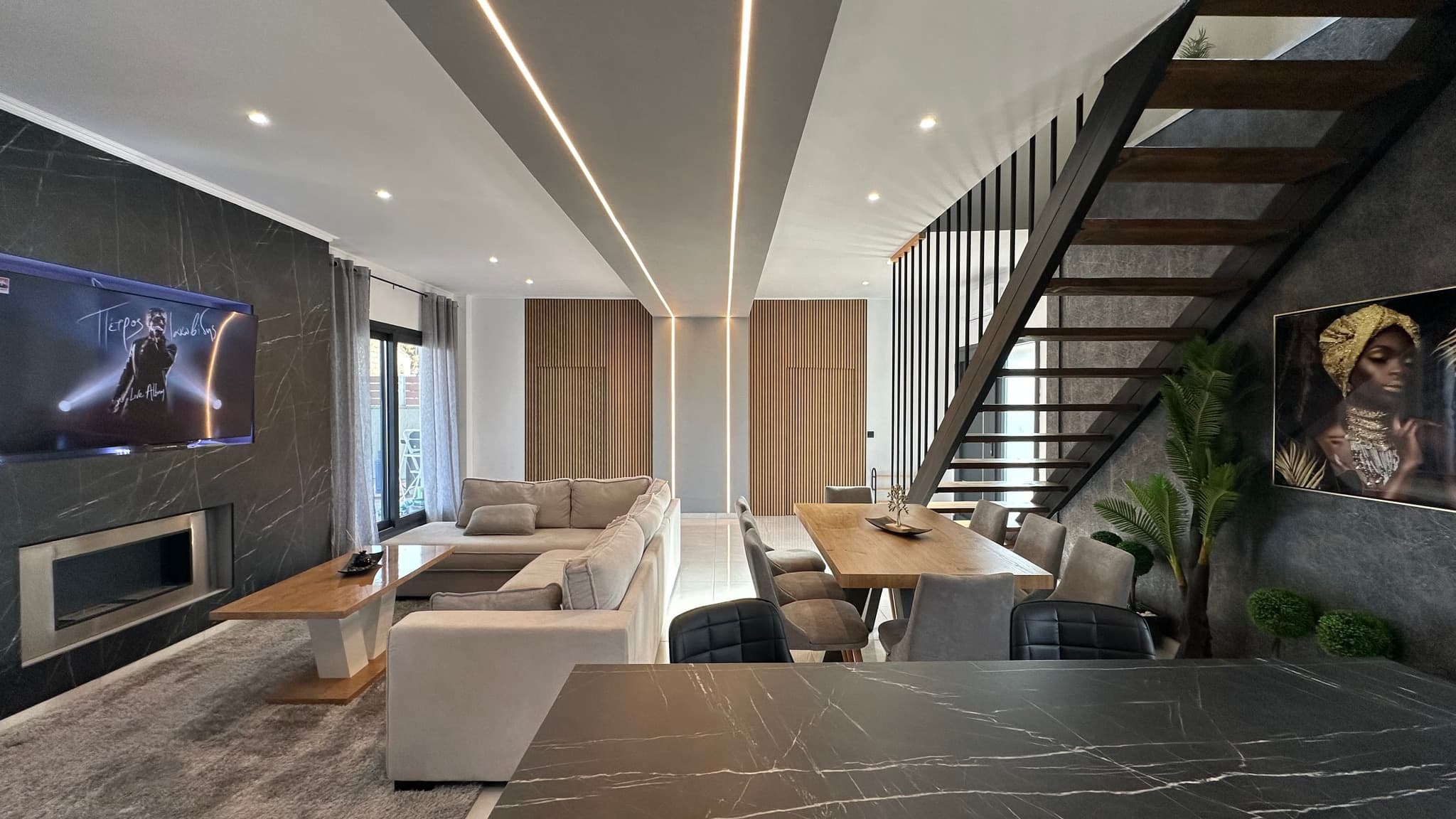 Open-plan living room with dark marble feature wall, wood accents, and linear lighting